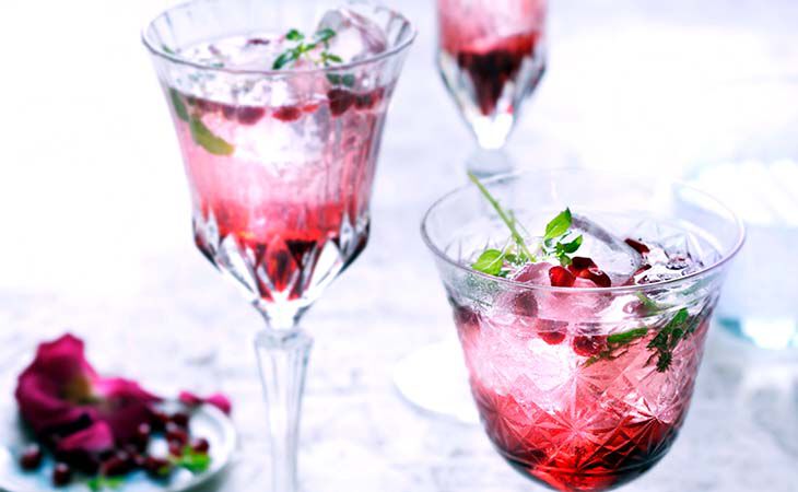 Elegant crystal glasses with pink pomegranate mocktail, ice and herbs, a refreshing alcohol-free cocktail recipe.